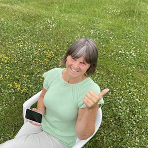 Kjersti Lium sitter i en stol og holder en mobiltelefon på en grønn gressbakke
