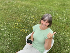 Kjersti Lium sitter i en stol og holder en mobiltelefon på en grønn gressbakke