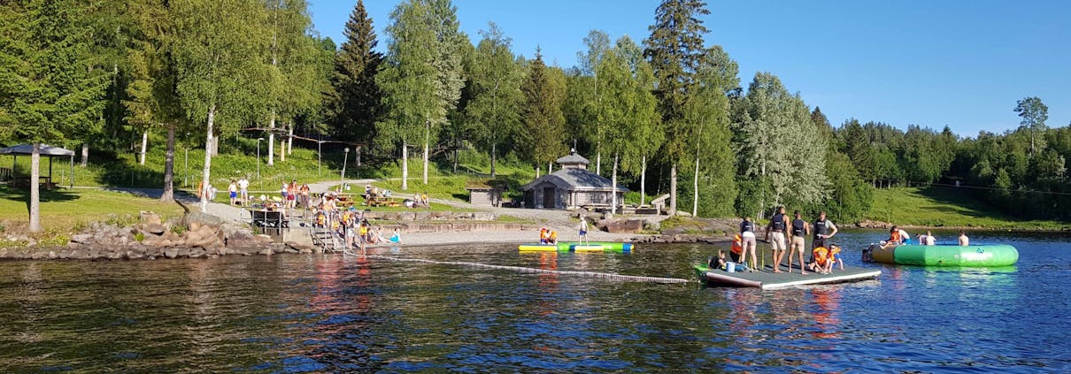 Strand ved Hurdalsjøen, mange mennesker er ute på en flåte