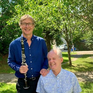 Georg Reiss står til venstre for Ulf Nilsen. Han holder i en klarinett, Ulf Nilsen sitter med et piano. Bildet er tatt utendørs.