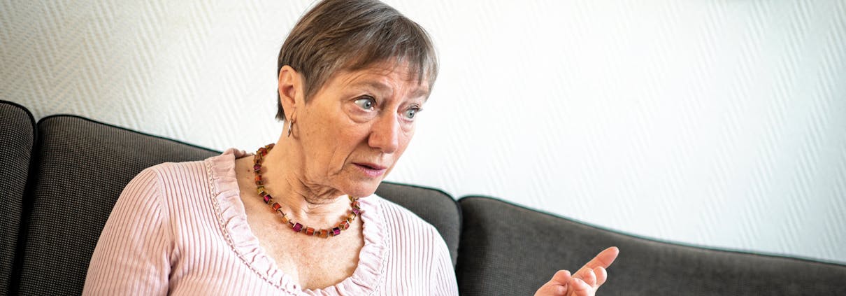 En dame sitter i en sofa og snakker. Hun peker ut i luften