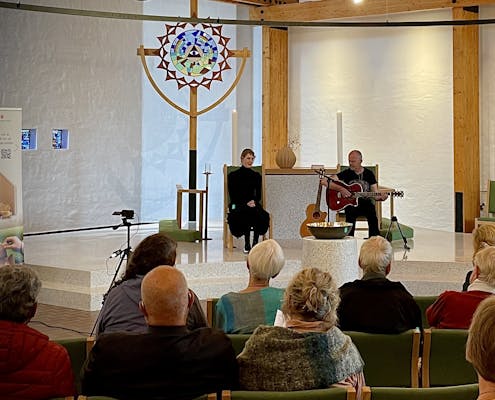 To personer sitter oppe ved et alter og spiller og synger.