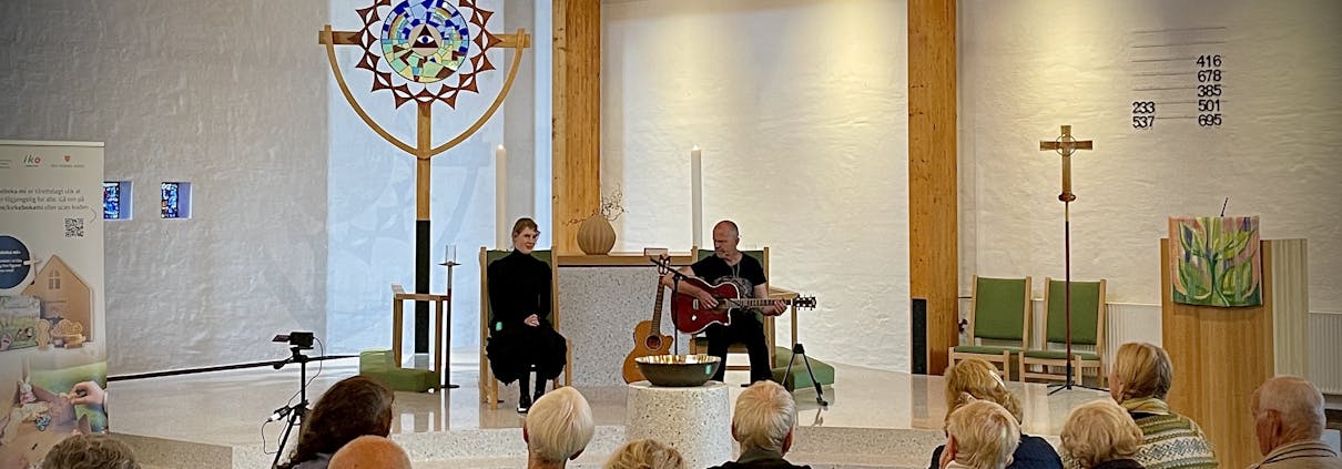 To personer sitter oppe ved et alter og spiller og synger.