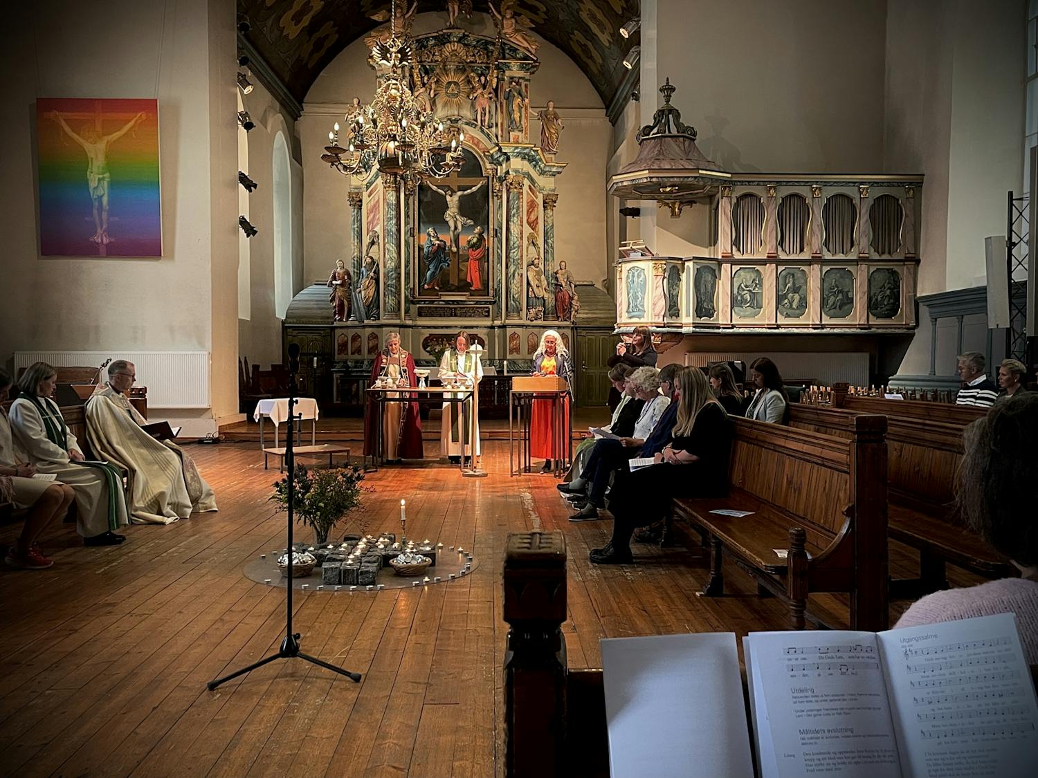 Bildet er tatt i Vår Frues kirke i Trondheim. Vi ser prester og andre kirkelige ansatte. En kvinne står ved en lespult og leser..