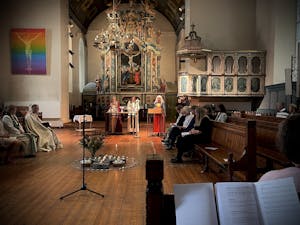 Bildet er tatt i Vår Frues kirke i Trondheim. Vi ser prester og andre kirkelige ansatte. En kvinne står ved en lespult og leser..