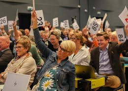 Menn og kvinner viser stemmetegn. De holder opp lapper med store tall på.