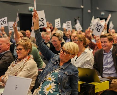 Menn og kvinner viser stemmetegn. De holder opp lapper med store tall på.