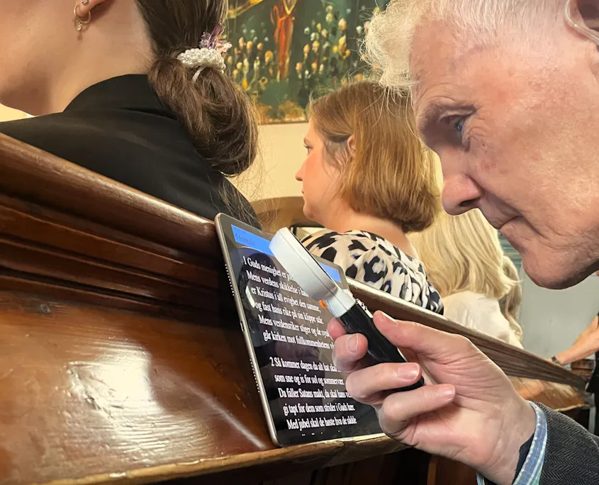 En mann holder opp en lupe foran en ipad og forsøker å lese en tekst.