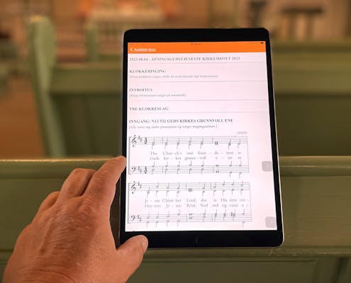 En nettbrett står i en kirke på skjermen ser vi en salme