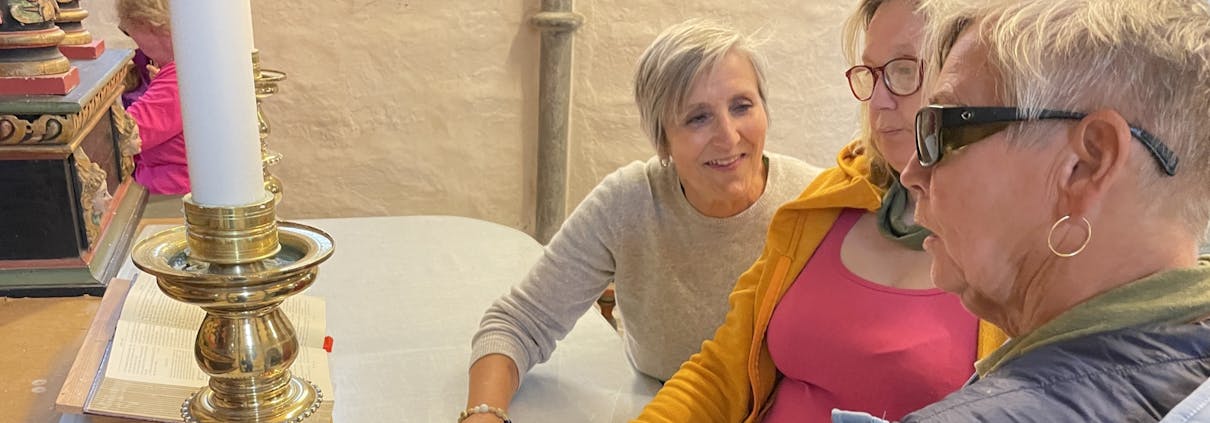 Tre kvinner står ved et kirkealter og kjenner på en lysestake .