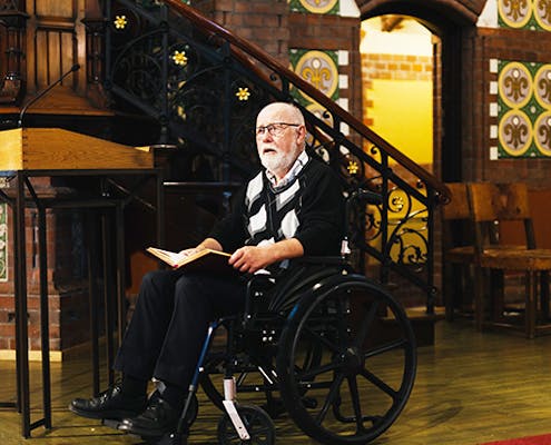 En mann sitter i en rullestol foran en prekestol i en kirke