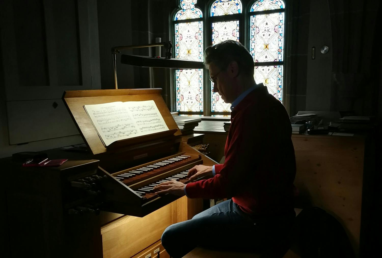 En kirkemusiker sitter og spiller på et orgel. Bak ham ser vi kirkekunst.