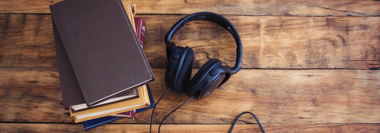 The Headphones and a Pile of Books lie on the Wooden Table.