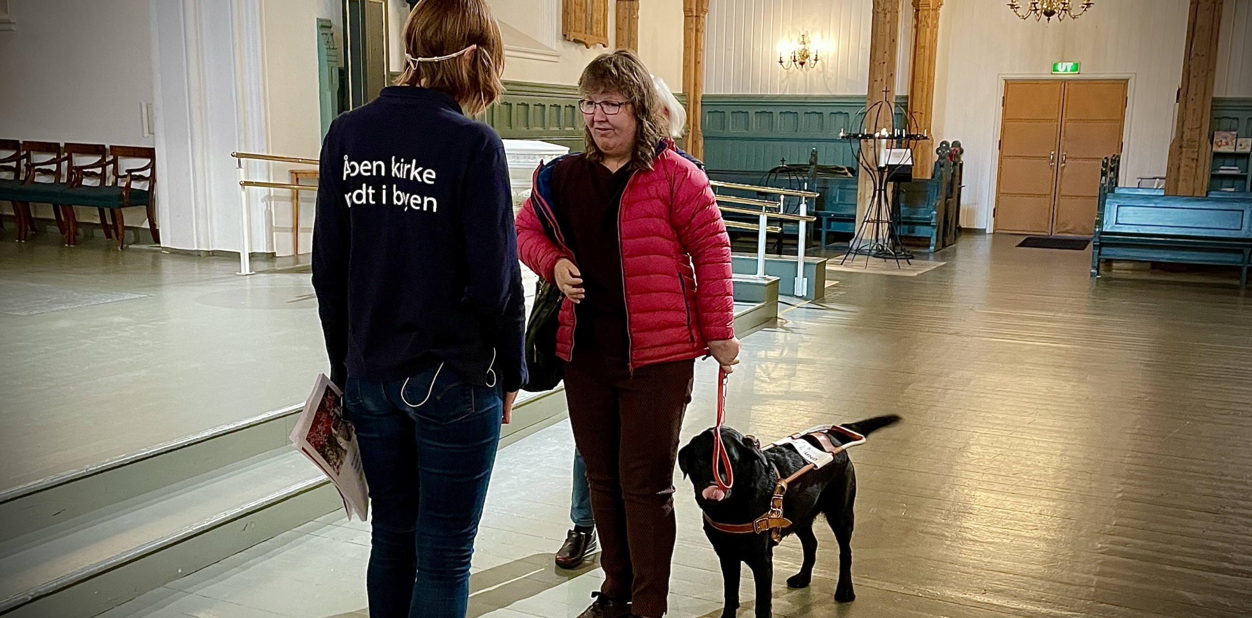 To personer snakker sammen - den ene har en førerhund. De er inne i en kirke.