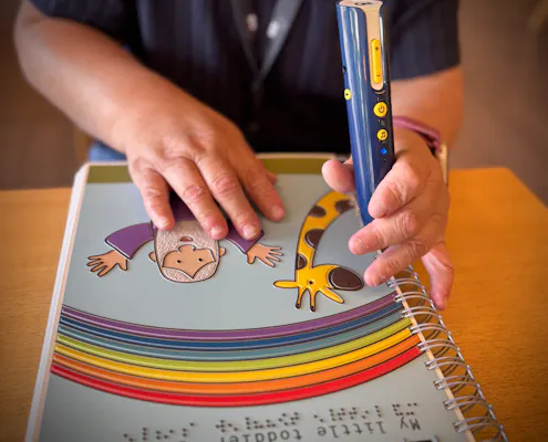 To hender kjenner på ei taktil bok og holder på en lesepenn